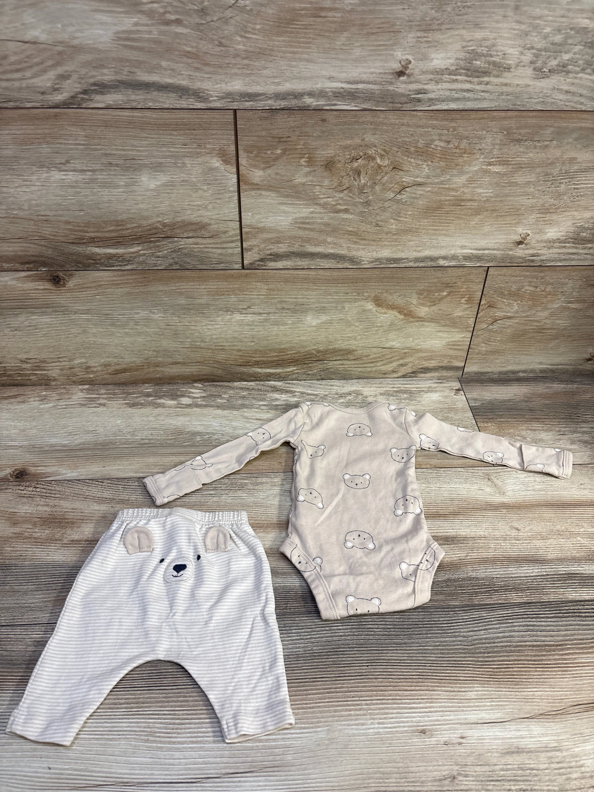 Flat lay of newborn beige 2-piece bear bodysuit and striped pants showcasing bear-face prints and elastic waist on wood