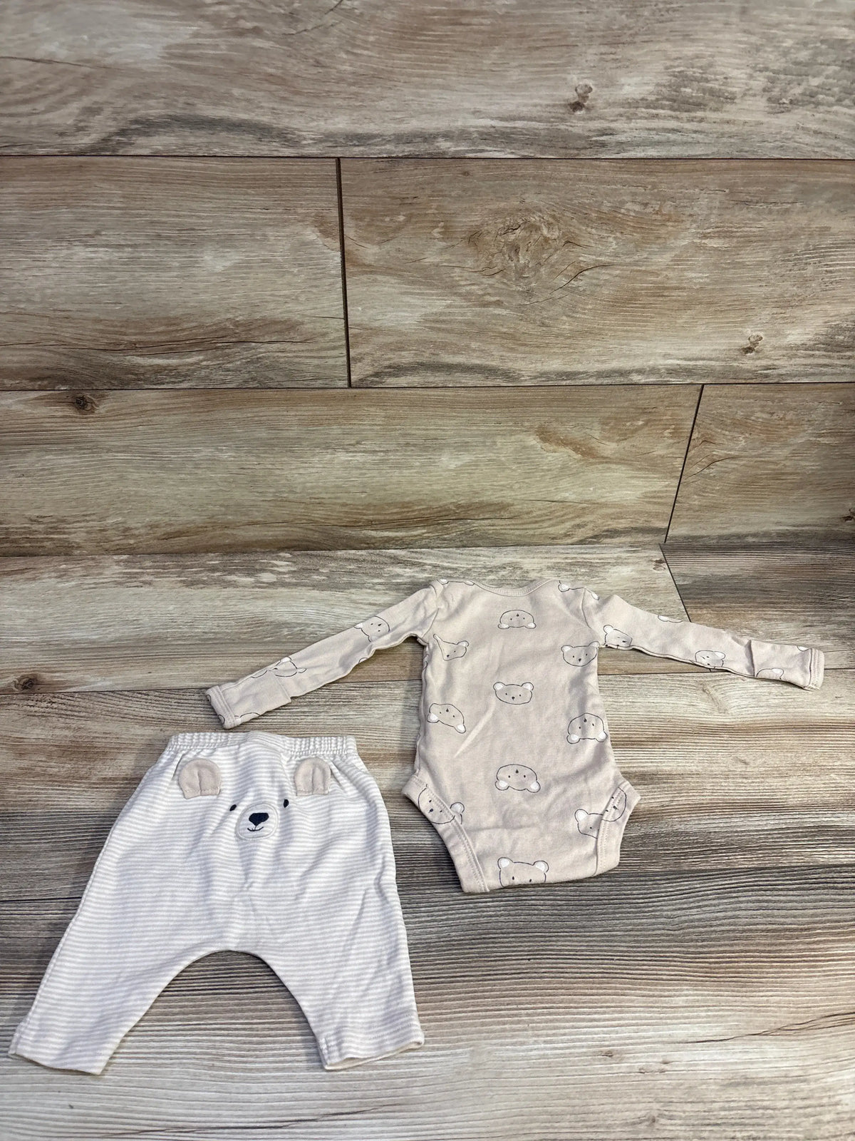 Flat lay of newborn beige 2-piece bear bodysuit and striped pants showcasing bear-face prints and elastic waist on wood
