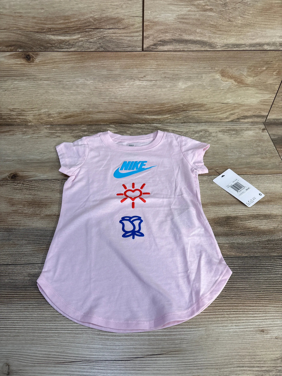 Front view of Nike t-shirt in pink foam, size 4T, showcasing a blue Nike logo and heart graphic on a wood background