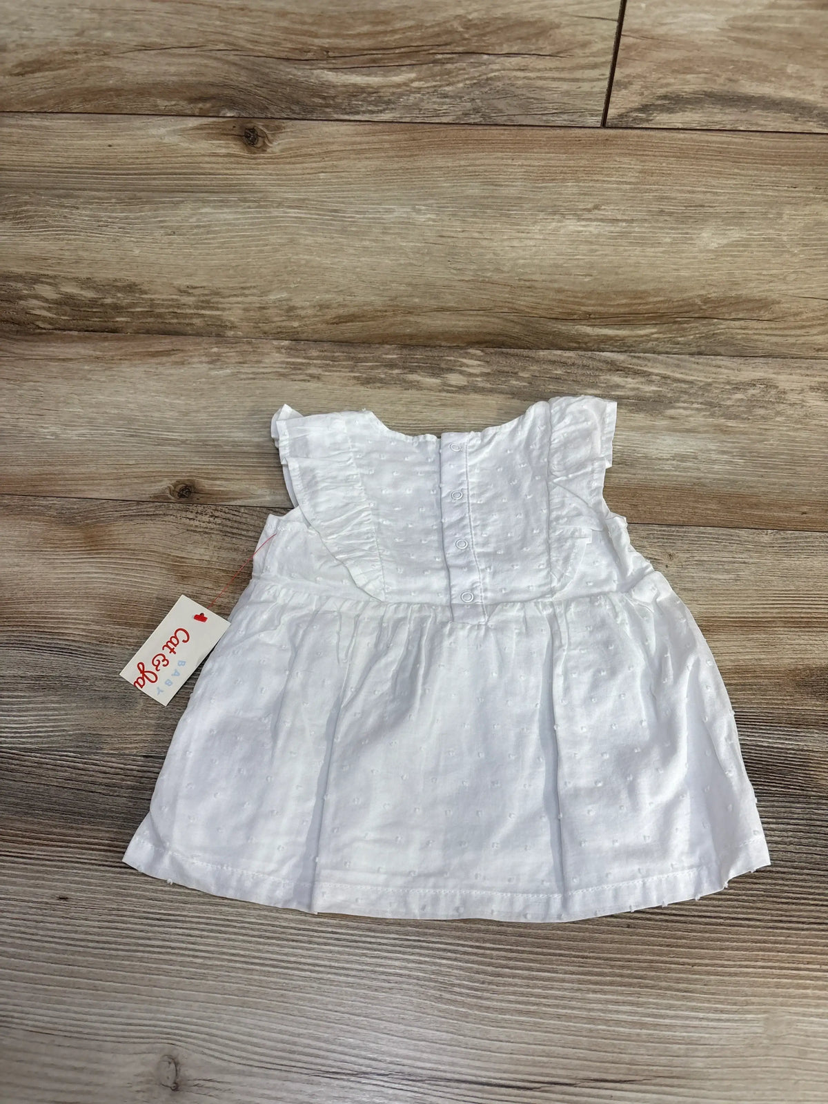 Flat lay of white Cat and Jack Swiss dot shirt in size 18 months showcasing flutter sleeves and back buttons on a wood floor