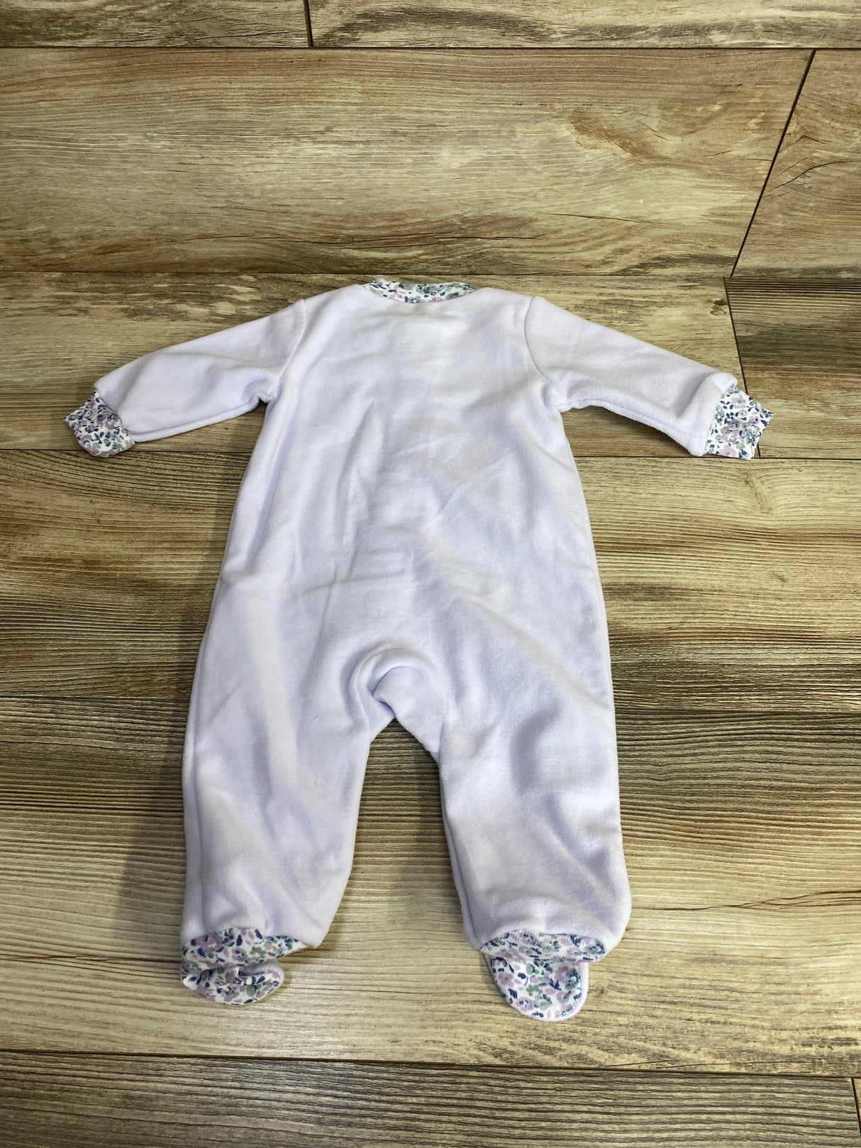 White baby sleeper with floral trim on sleeves, collar, and feet laid on wooden floor
