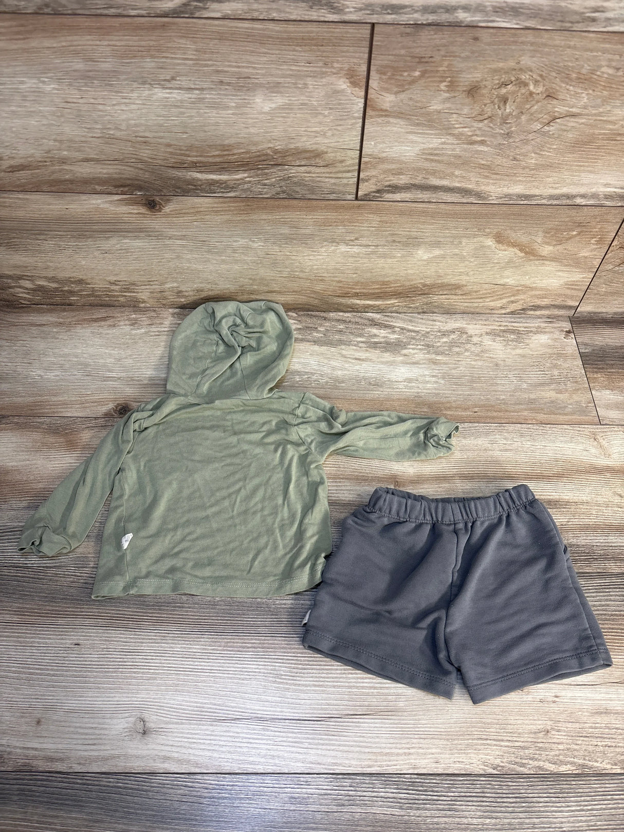 Green hooded long sleeve toddler shirt and gray shorts set on wood floor