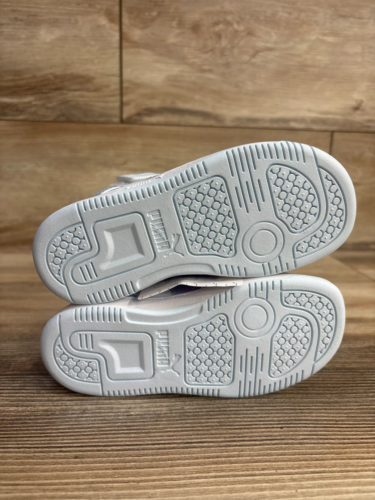 White Puma sneakers with textured rubber soles on wooden floor background