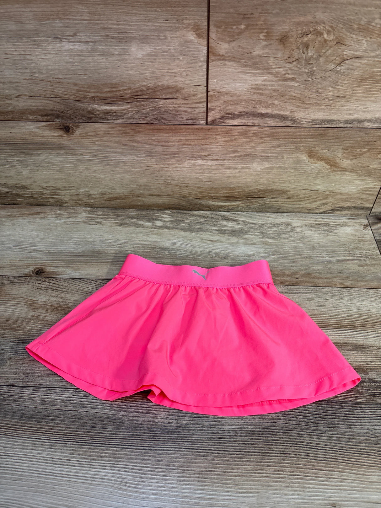 Flat lay of pink Puma moisture-wicking skort size 3T with elastic waistband, Puma logo and inner shorts on wood background