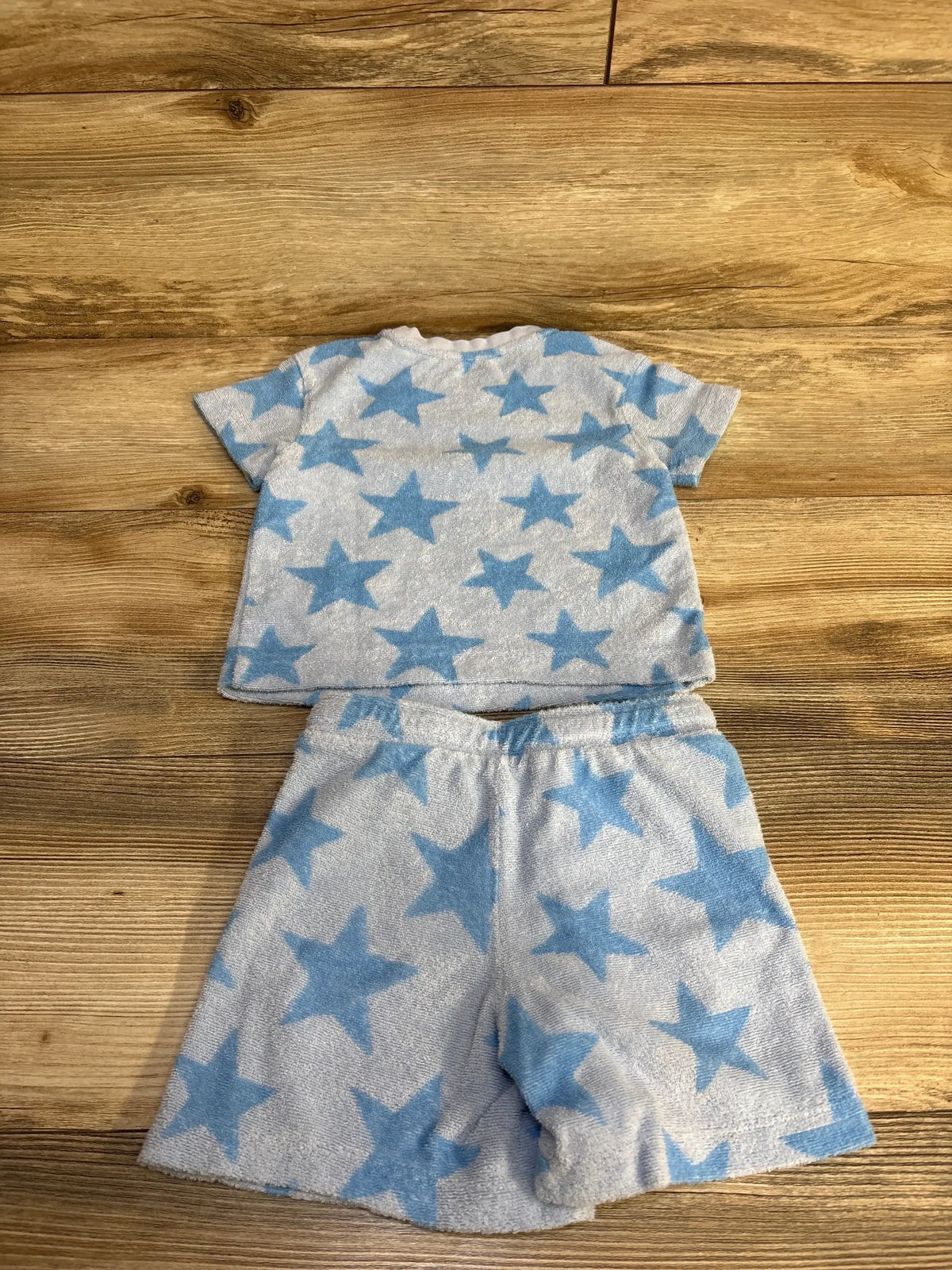 Flat-lay of toddler terry cloth two-piece set with short-sleeve shirt and elastic-waist shorts, blue star print on wood background