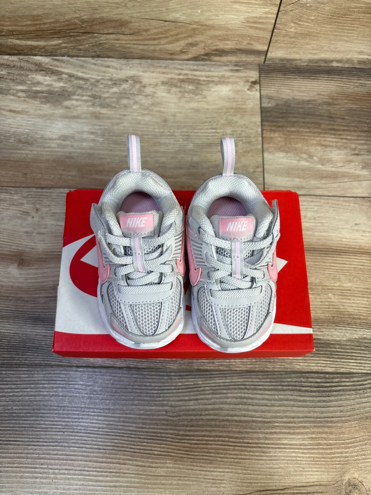 Top view of Nike Vomero 5 TD toddler sneakers showcasing grey mesh uppers, pink Swoosh accents and pull tabs on a red Nike box