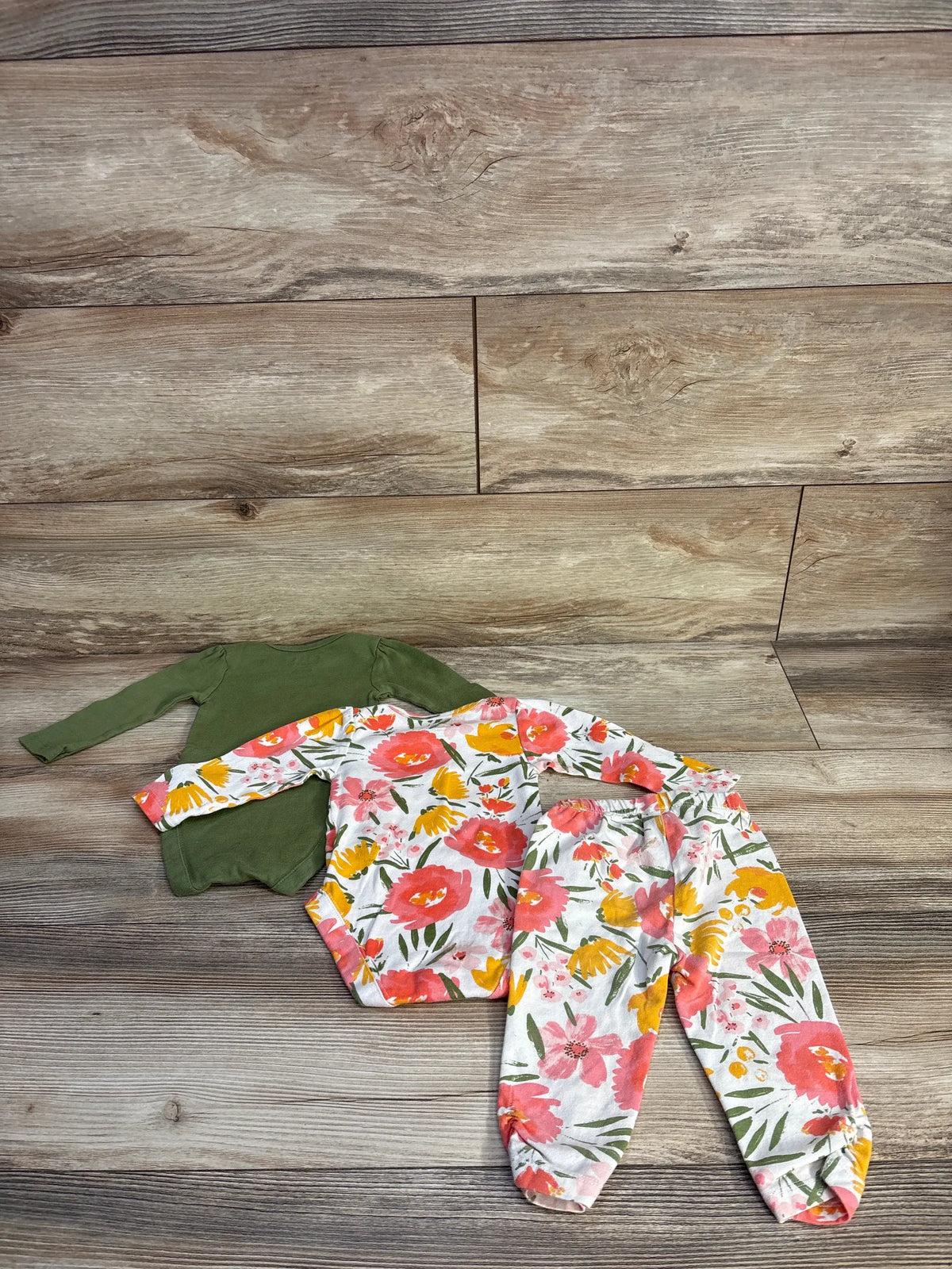 Flat lay of Children’s Place three-piece bodysuit and pant set with green and white floral pieces on wood flooring