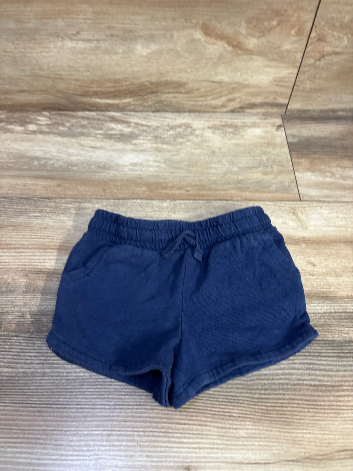 Flat lay of navy Jumping Beans toddler drawstring shorts showing elastic waistband with tie and front pockets on wood floor