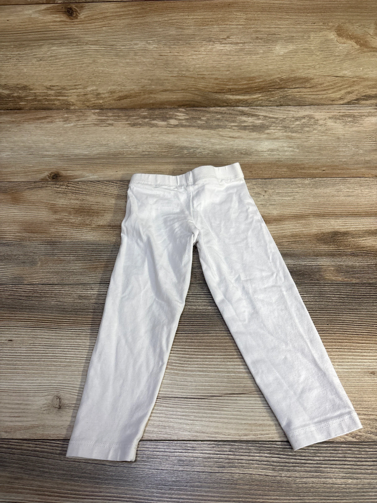 Flat lay of white Children’s Place toddler leggings size 2T showing elastic waistband and straight legs on wood background