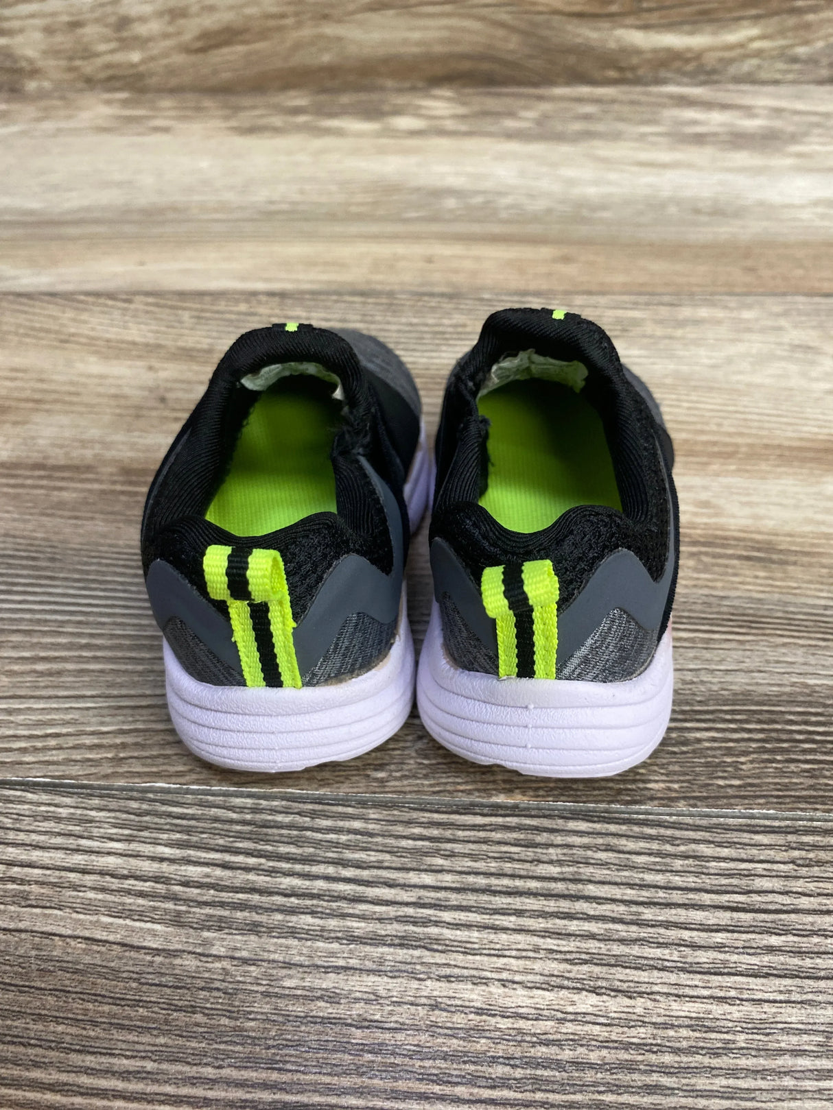 Pair of kids sneakers, black and gray with neon yellow trim, on wood floor