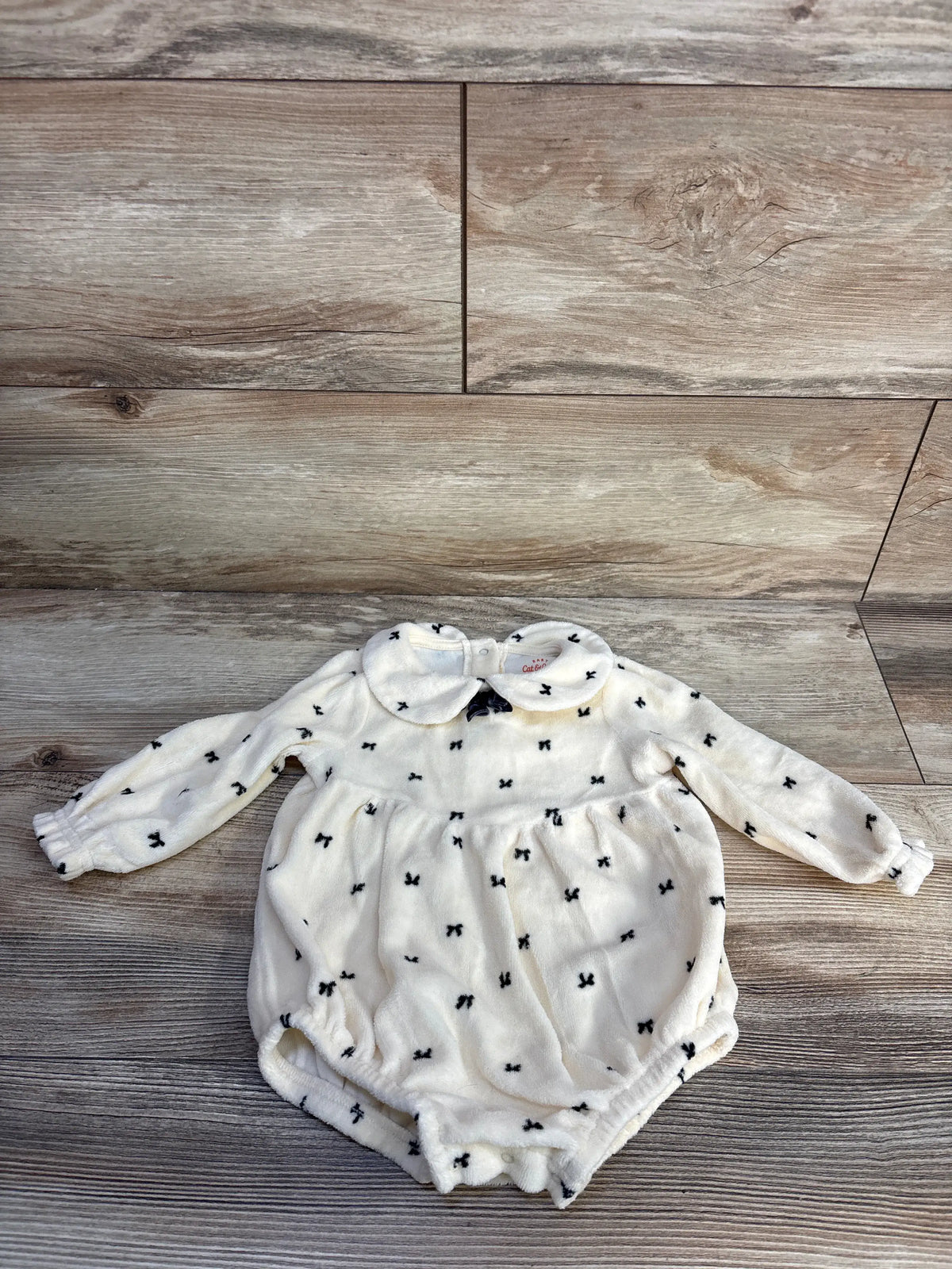 Front view of Cat & Jack ivory collared long sleeve bubble romper showcasing black bow pattern with wood grain background