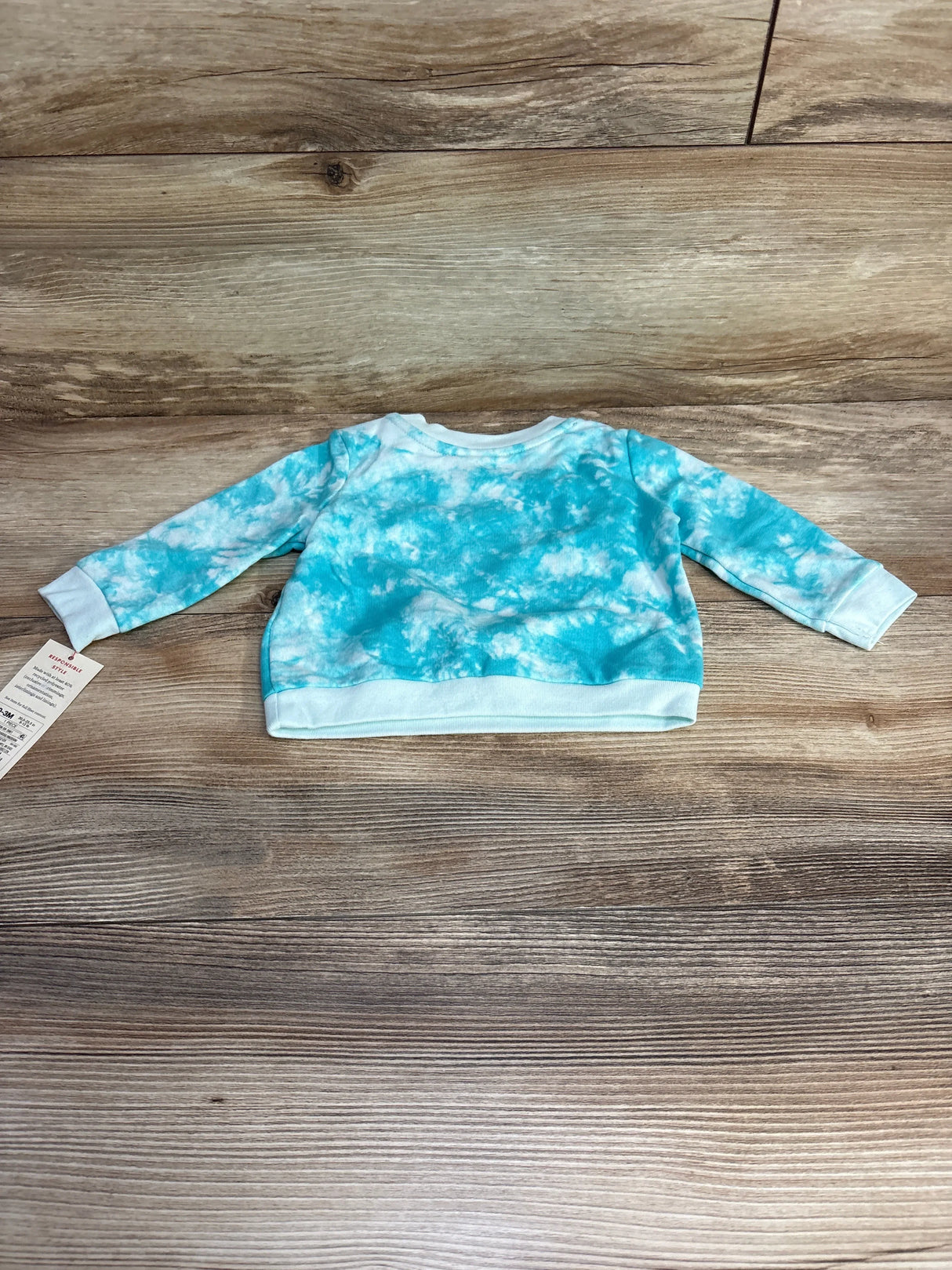 Flat lay of newborn Cat & Jack blue tie-dye sweatshirt showing long sleeves and ribbed cuffs and hem on wood plank background