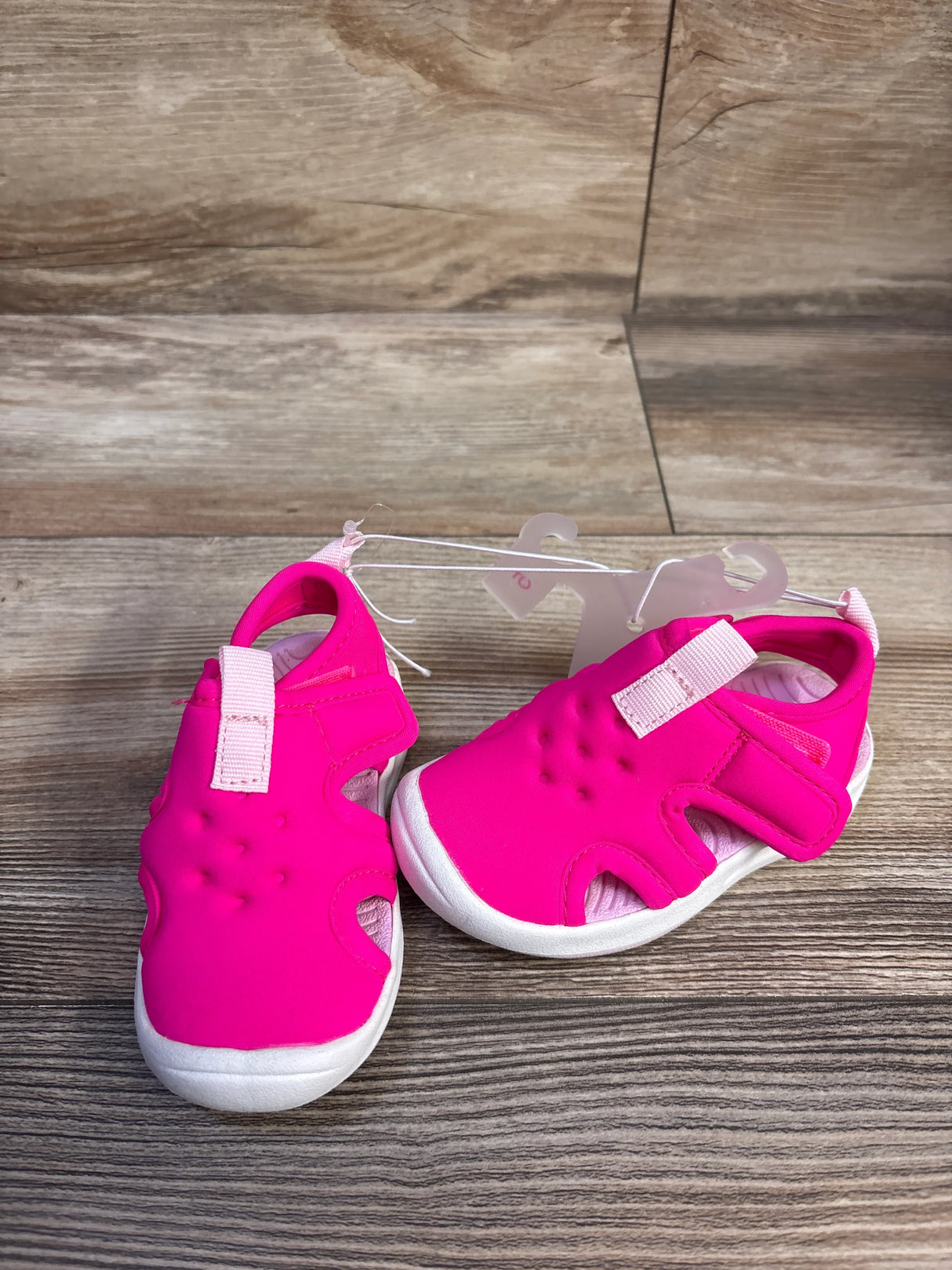 Three-quarter view of Cat & Jack water shoes size 5C, bright pink upper with velcro strap and white sole on wood background