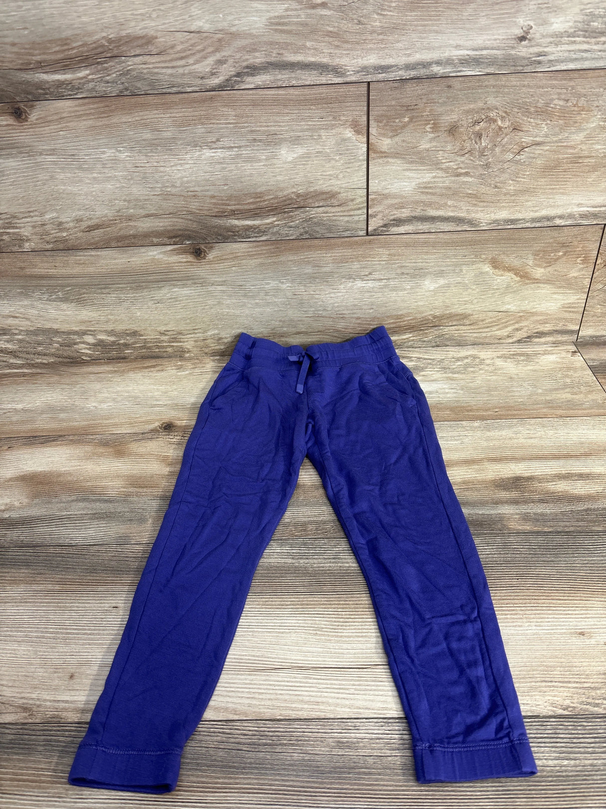 Purple children's jogger pants with elastic waistband and drawstring on wood floor background
