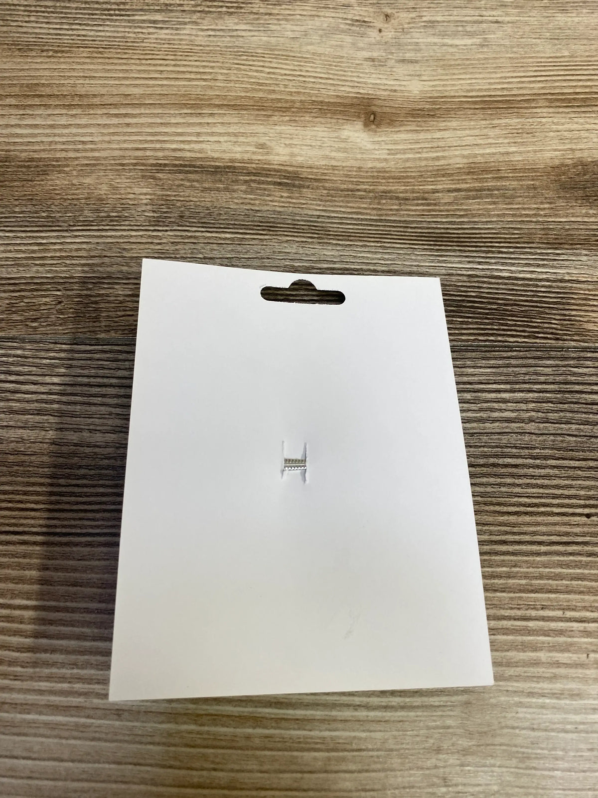 Blank white product tag with hang hole on wood surface, ready for kids or maternity item labeling