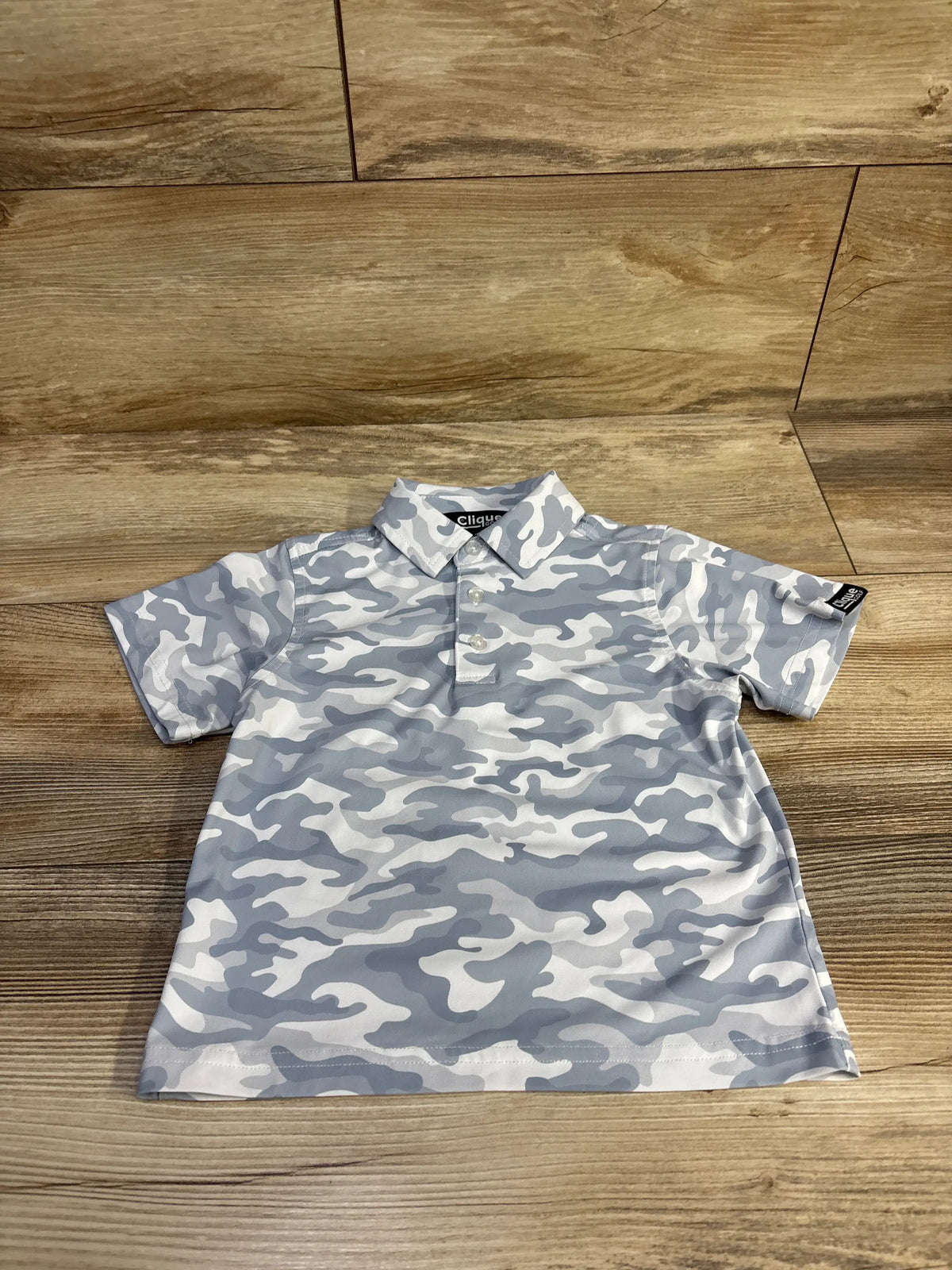 Front view of Clique Golf camo polo shirt, size 2T, with gray-white camouflage and short sleeves on wood flooring