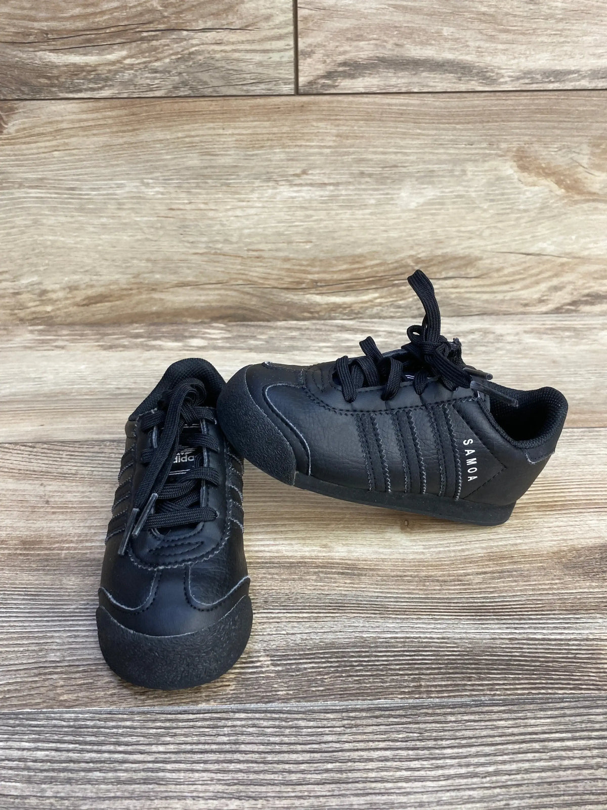 Black Adidas Samoa sneakers on wood floor, classic leather shoes with laces