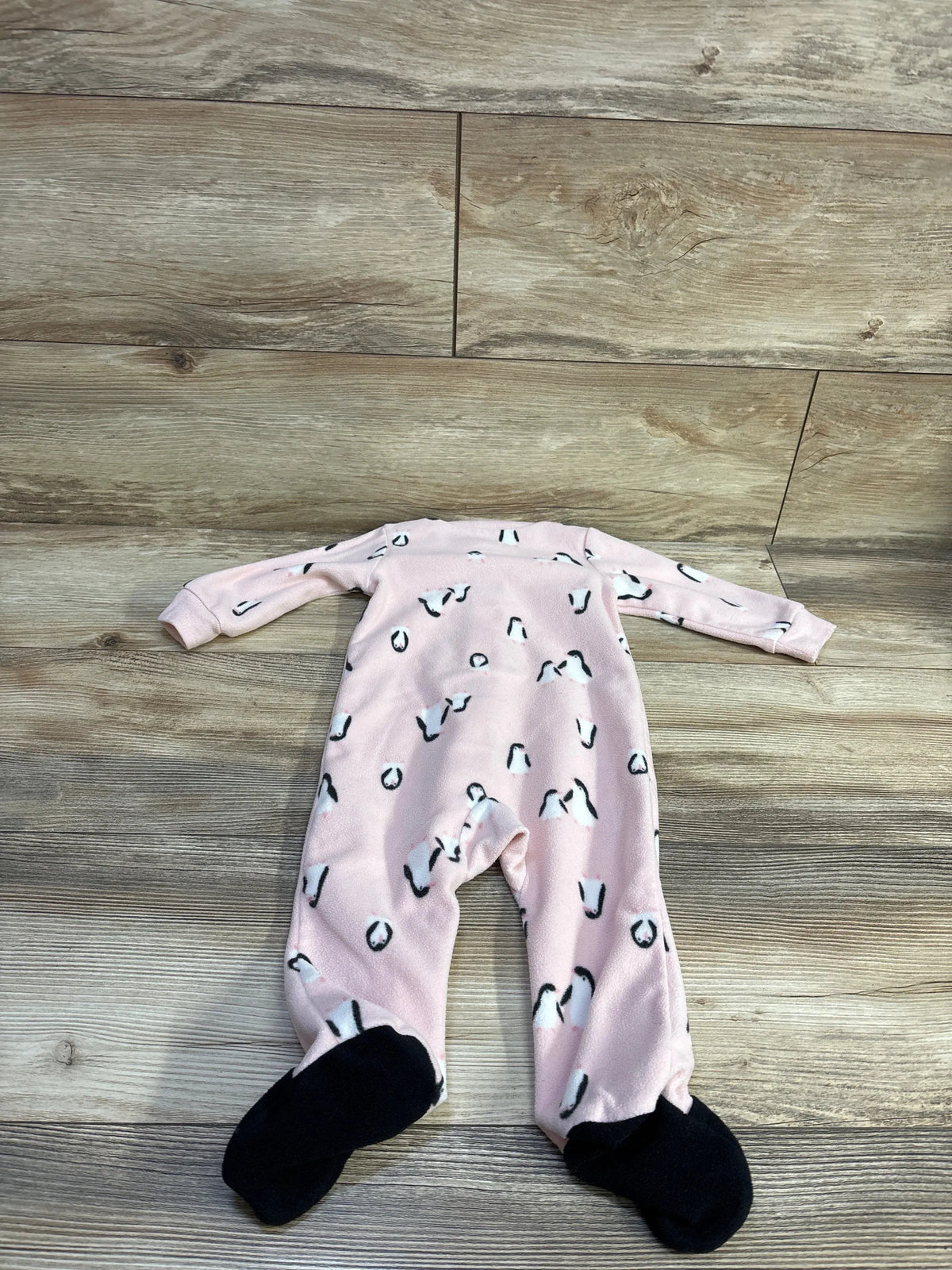 Flat-lay of Carter’s pink 9-month blanket sleeper showing penguin print and black footed soles on wood floor