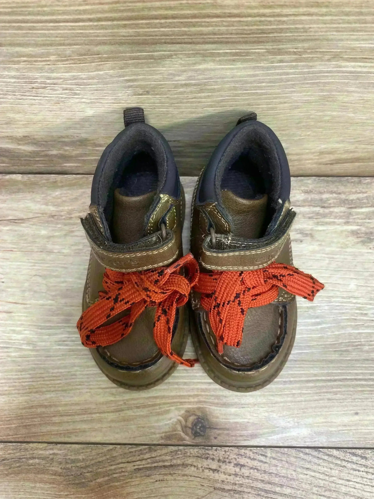 Top view of Carter’s Norman toddler brown ankle boots showcasing bright orange laces and Velcro strap on wood background
