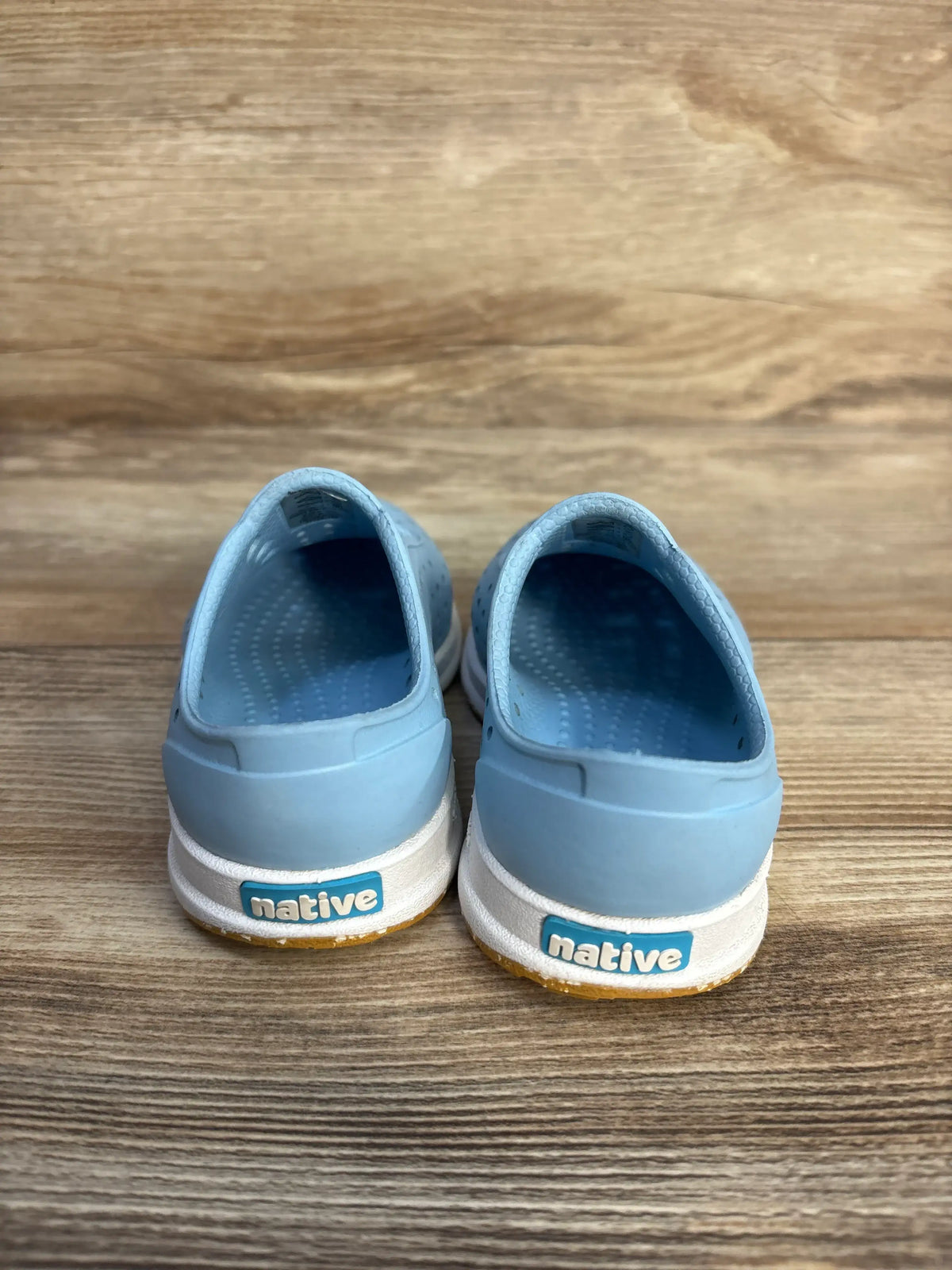 Rear view of blue Native Robbie Sugarlite slip-on shoes for kids on a wooden surface.