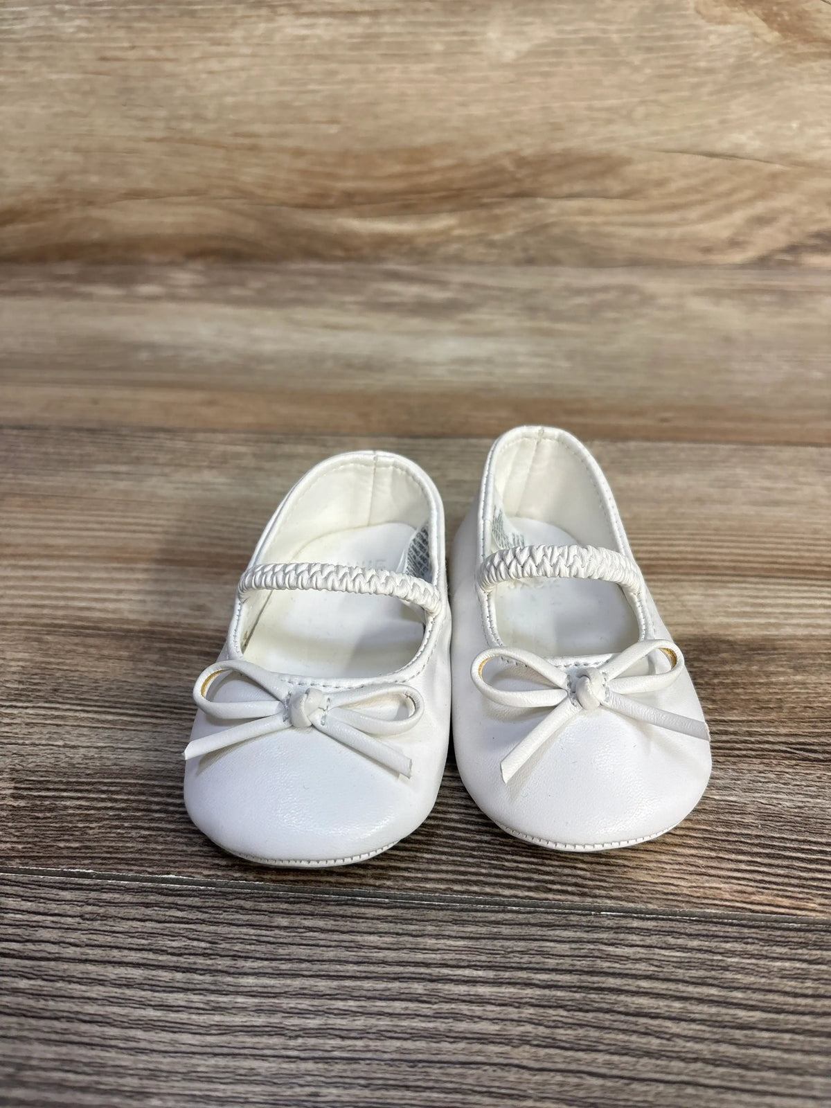 Pair of white Me n Mommy To Be bow soft sole ballet flats for toddlers on a wood surface