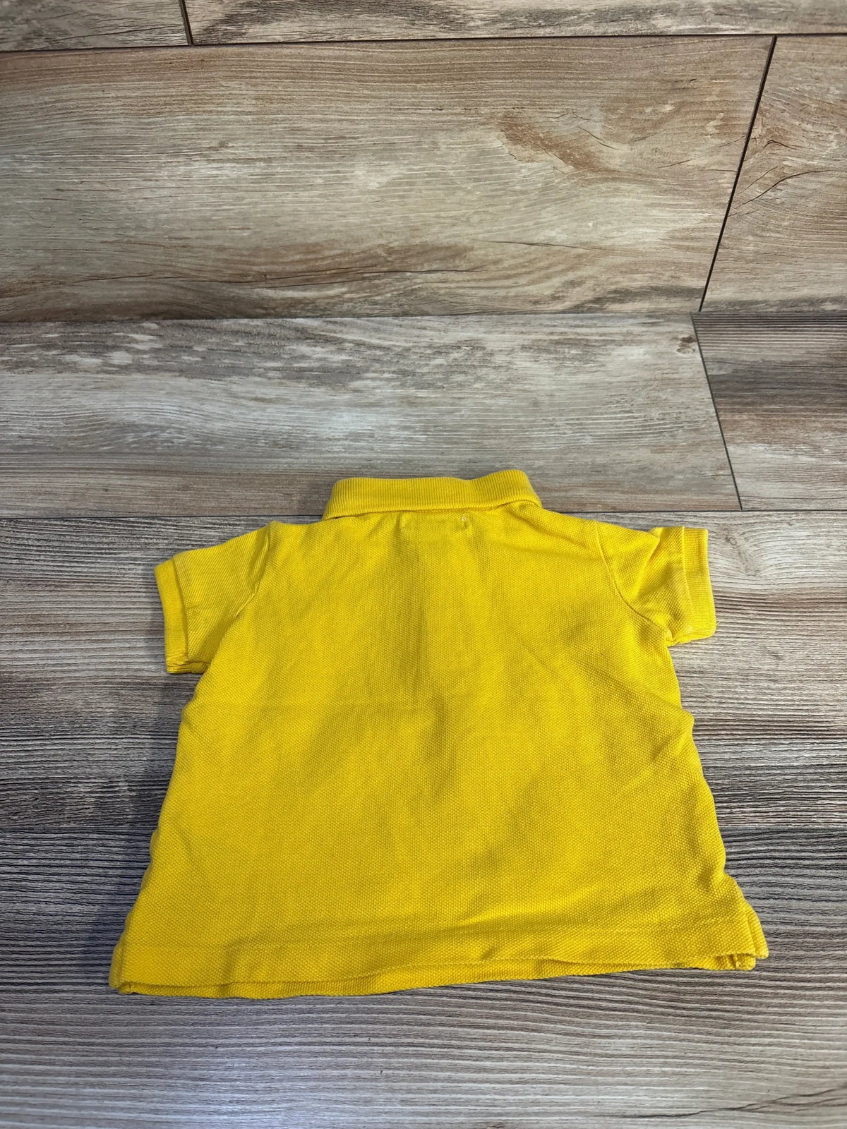 Back view of yellow Ralph Lauren baby polo shirt size 6M showing short sleeves and ribbed collar on wood floor background