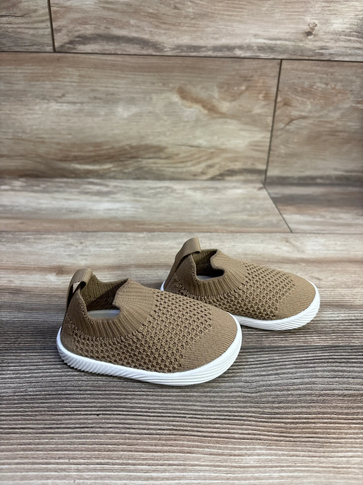 Front three-quarter view of brown knit toddler sock sneakers showcasing white non-slip sole and heel pull tab on wood background