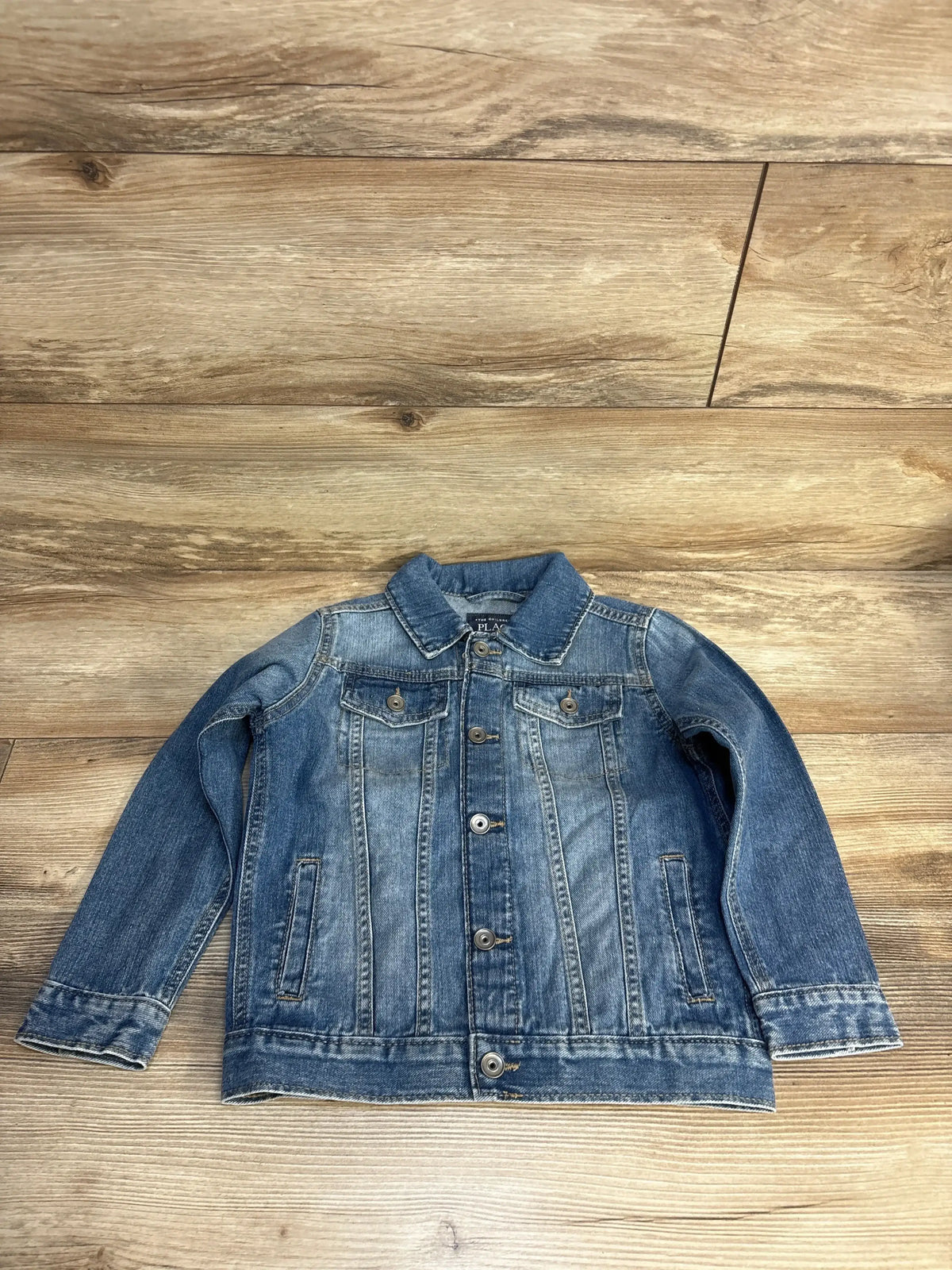Kids denim jacket with button front and chest pockets, laid on wood floor