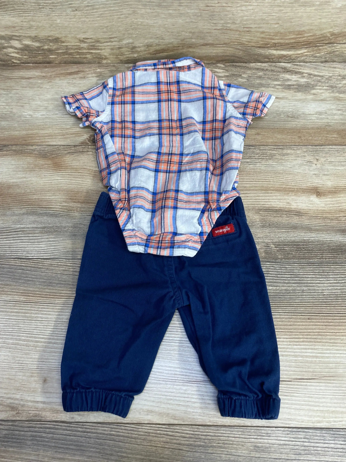 Flat lay of baby plaid bodysuit and navy Wrangler pants showing elastic ankle cuffs on light wood background