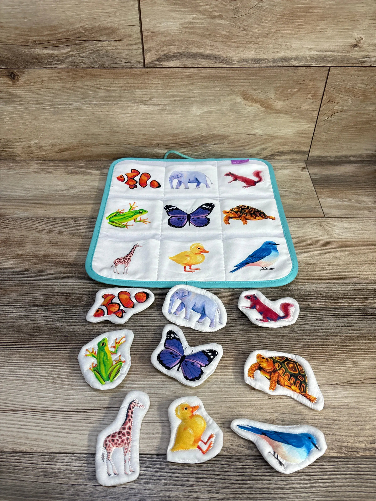 Front view of Lovevery Quilted Critter Pockets showcasing nine animal pockets and matching cotton critters on a wood floor