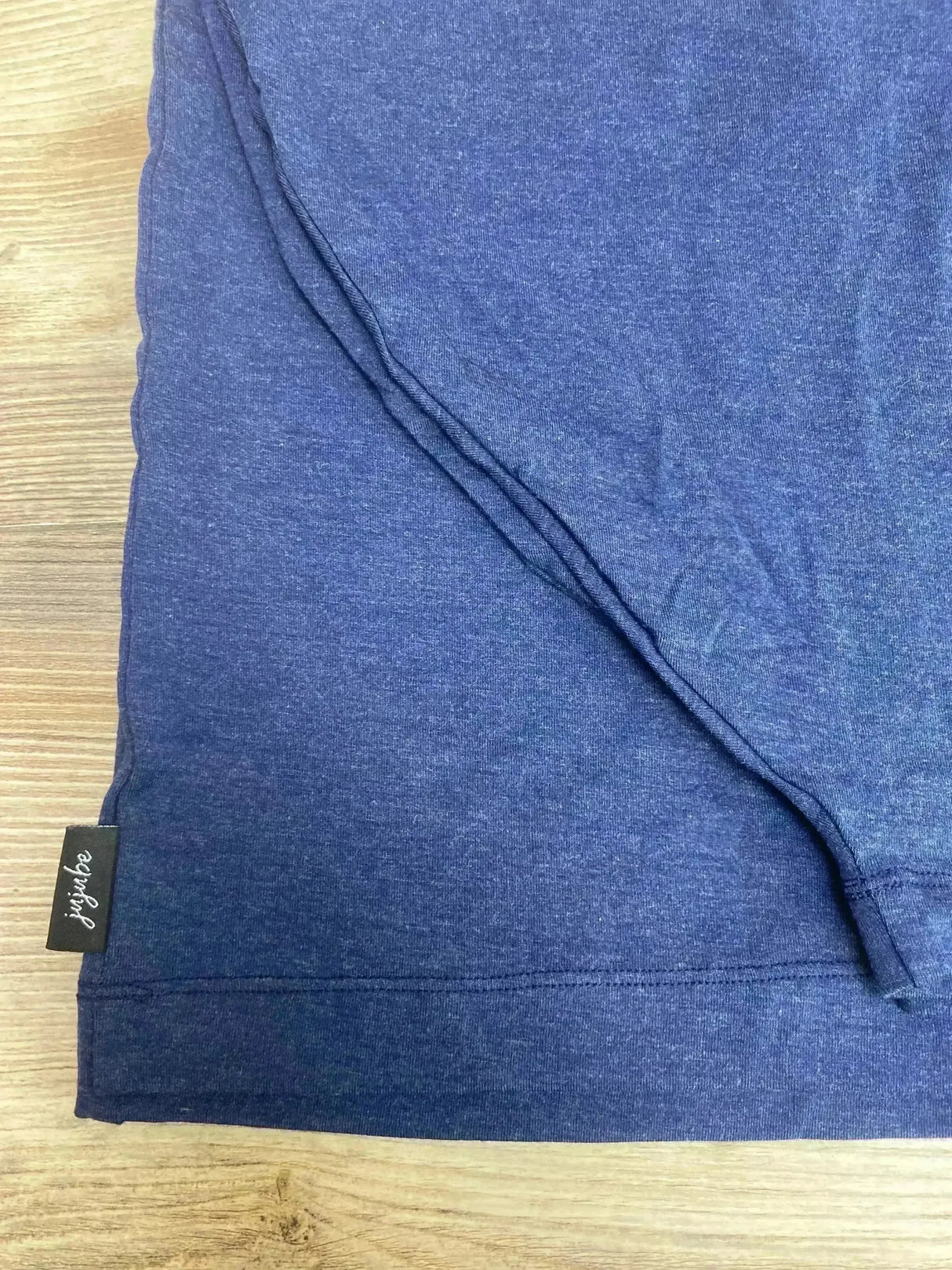 Close-up of Jujube 6-in-1 car seat cover showing navy heather fabric, hem stitching, and brand tag on wood background