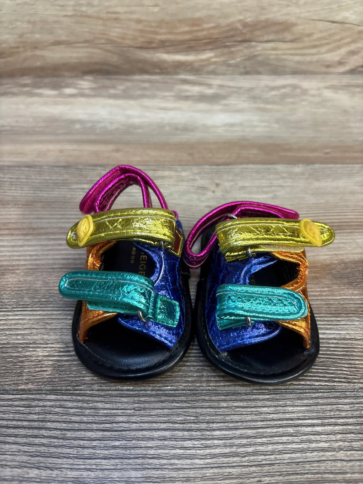 Front view of Kurt Geiger London Orson metallic leather toddler sandals size 2C showcasing multicolored velcro straps on wooden background