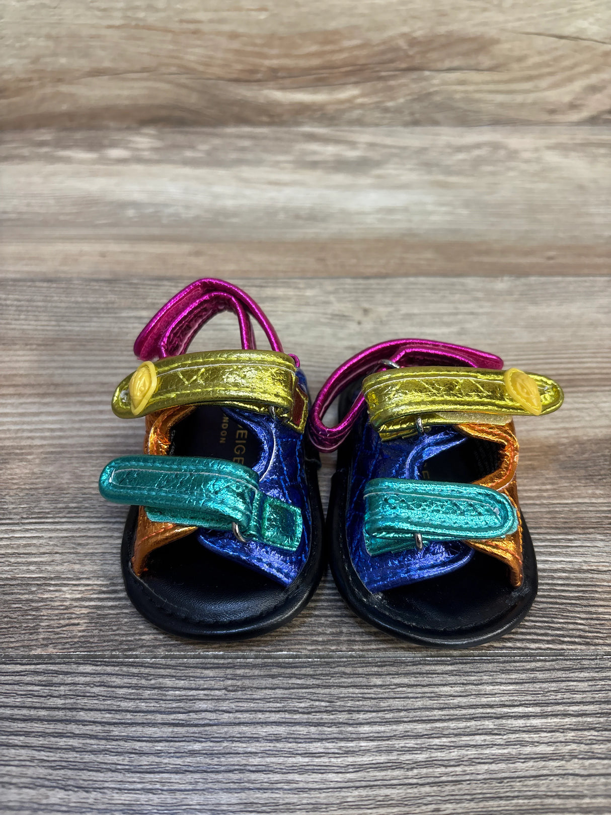 Colorful metallic toddler sandals with velcro straps on wood background
