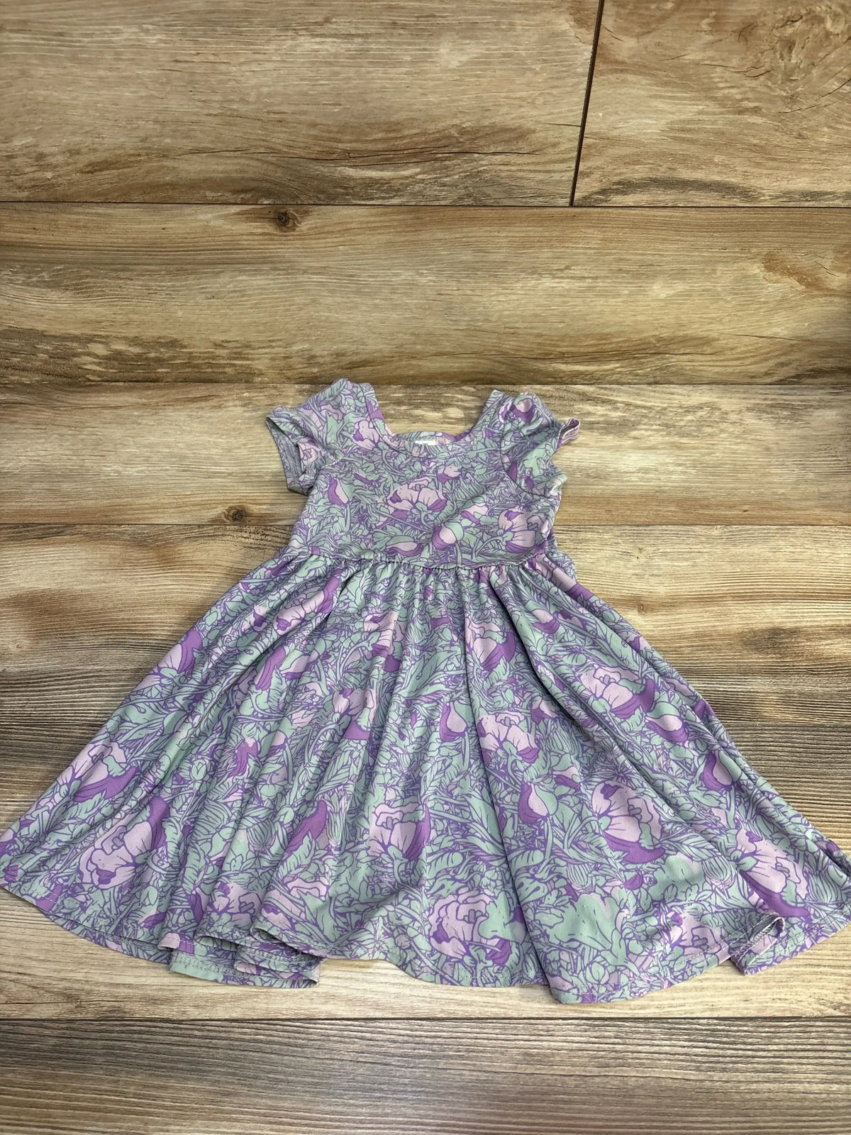Flat lay of purple 2T short-sleeve toddler dress with all-over floral pattern and gathered skirt on wood floor