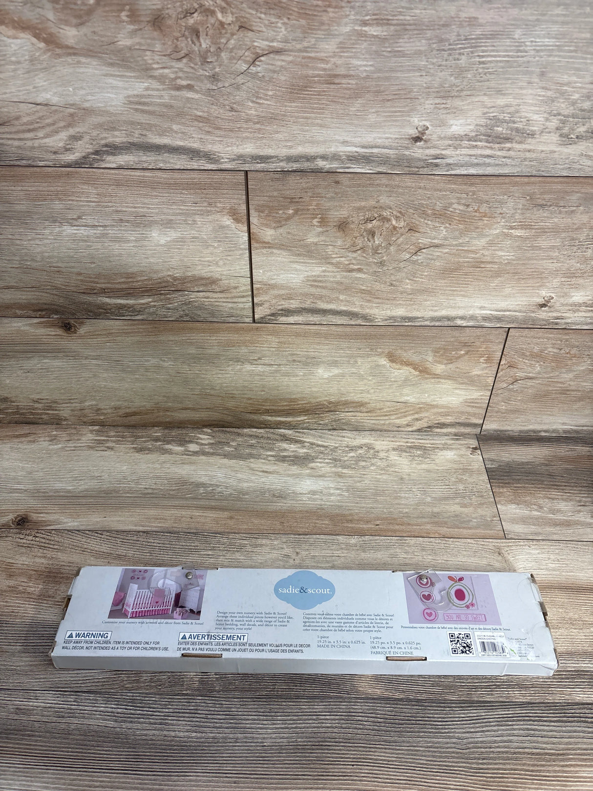 Sadie & Scout baby crib wall decor packaging with pink hearts on wood floor