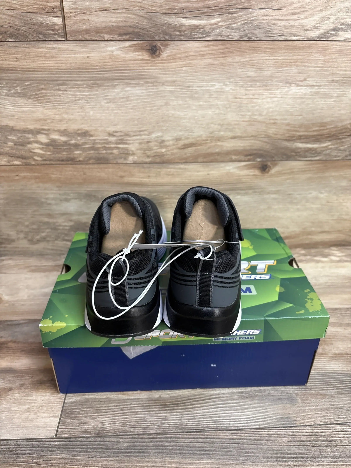 Black athletic sneakers on a Skechers memory foam shoebox, wood floor background