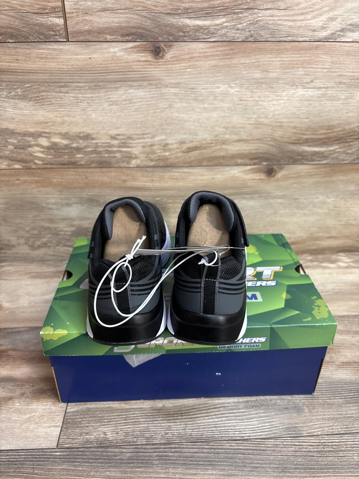 Black athletic sneakers on a Skechers memory foam shoebox, wood floor background