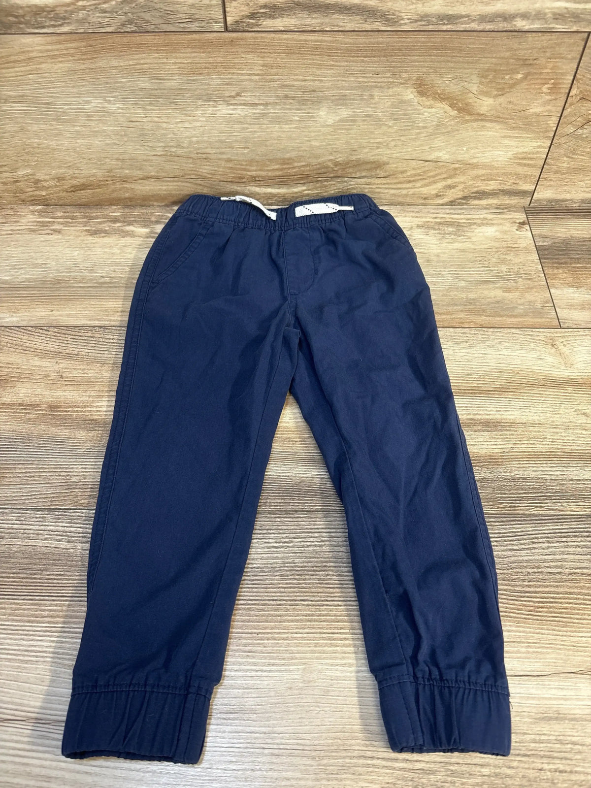 Navy blue kids jogger pants with elastic waist and cuffs, laid flat on wood floor