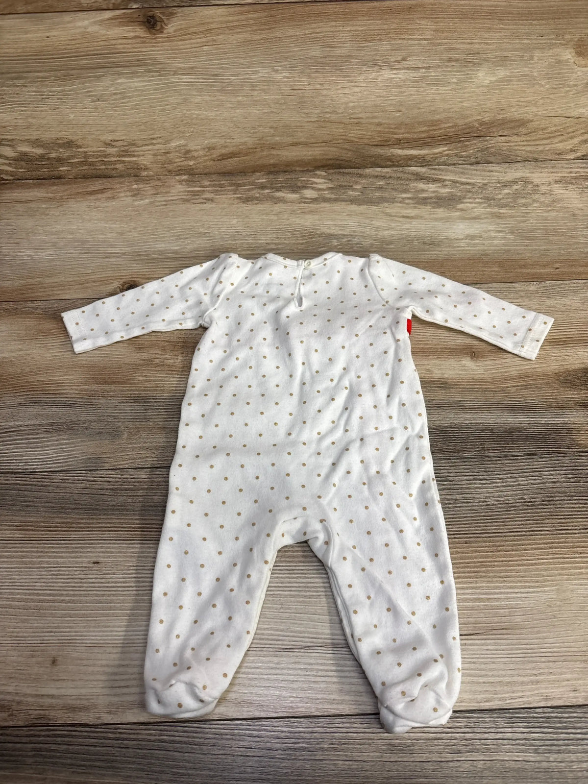 White baby onesie with gold polka dots, laid on wooden surface