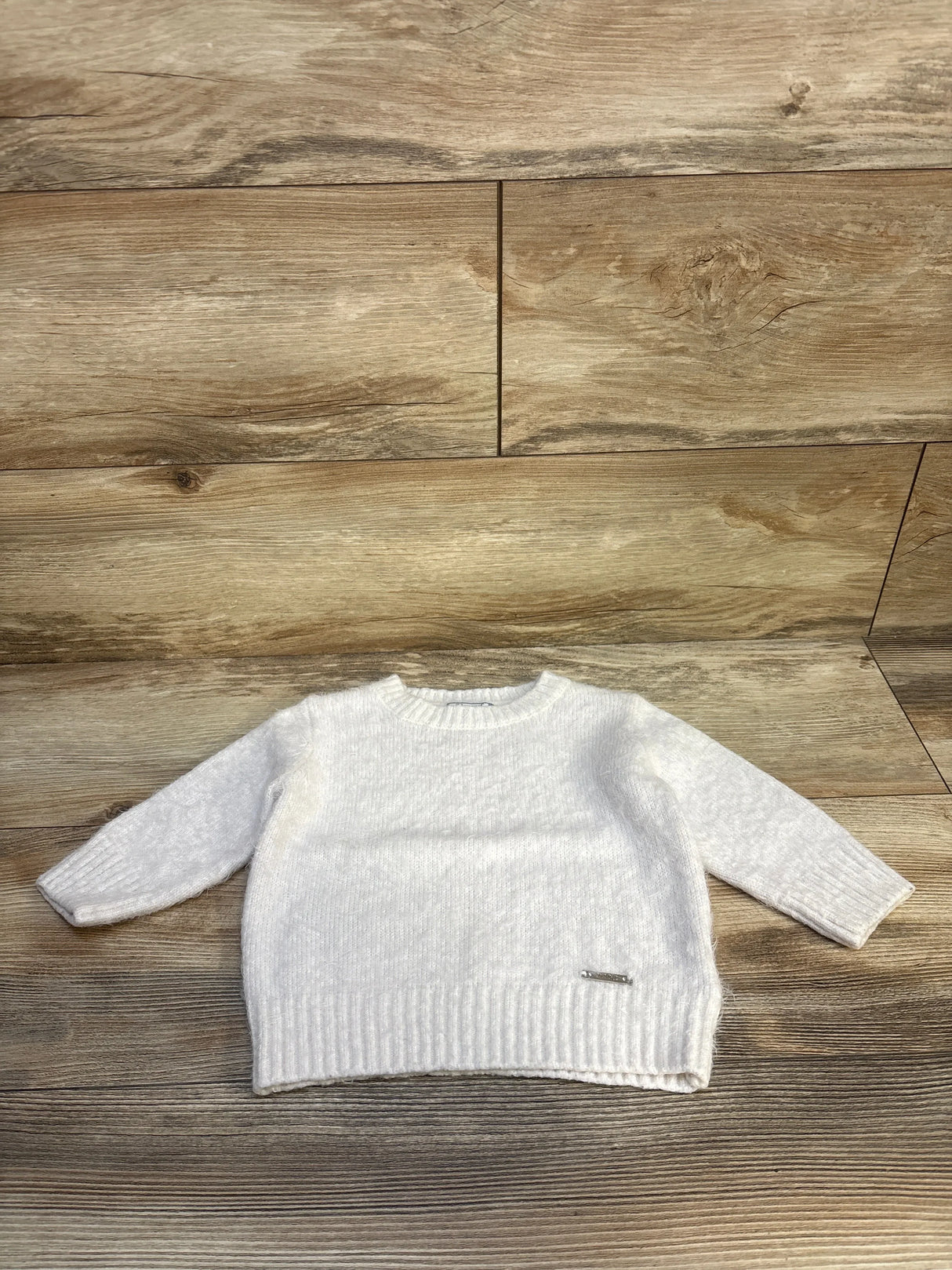 White long sleeve knit baby sweater on wood background, gently used kids clothing
