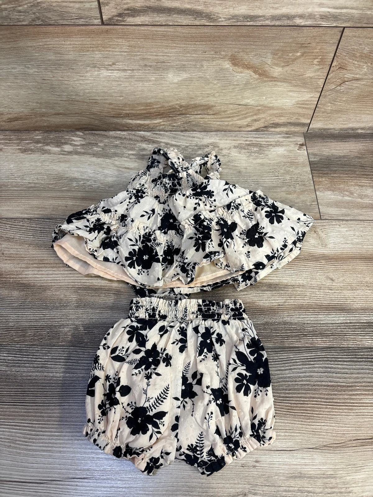 Flat lay of Haute Hippie cream smocked top and shorts set showcasing black floral print with wood-look flooring