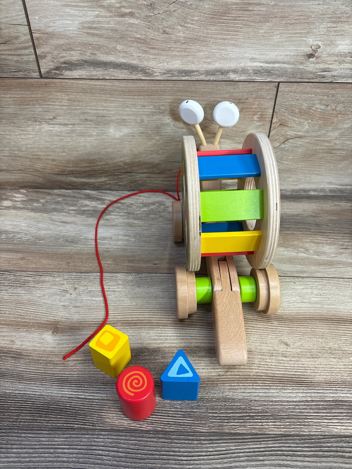Wooden colorful pull-along snail toy with a red string and three shape blocks on wood floor