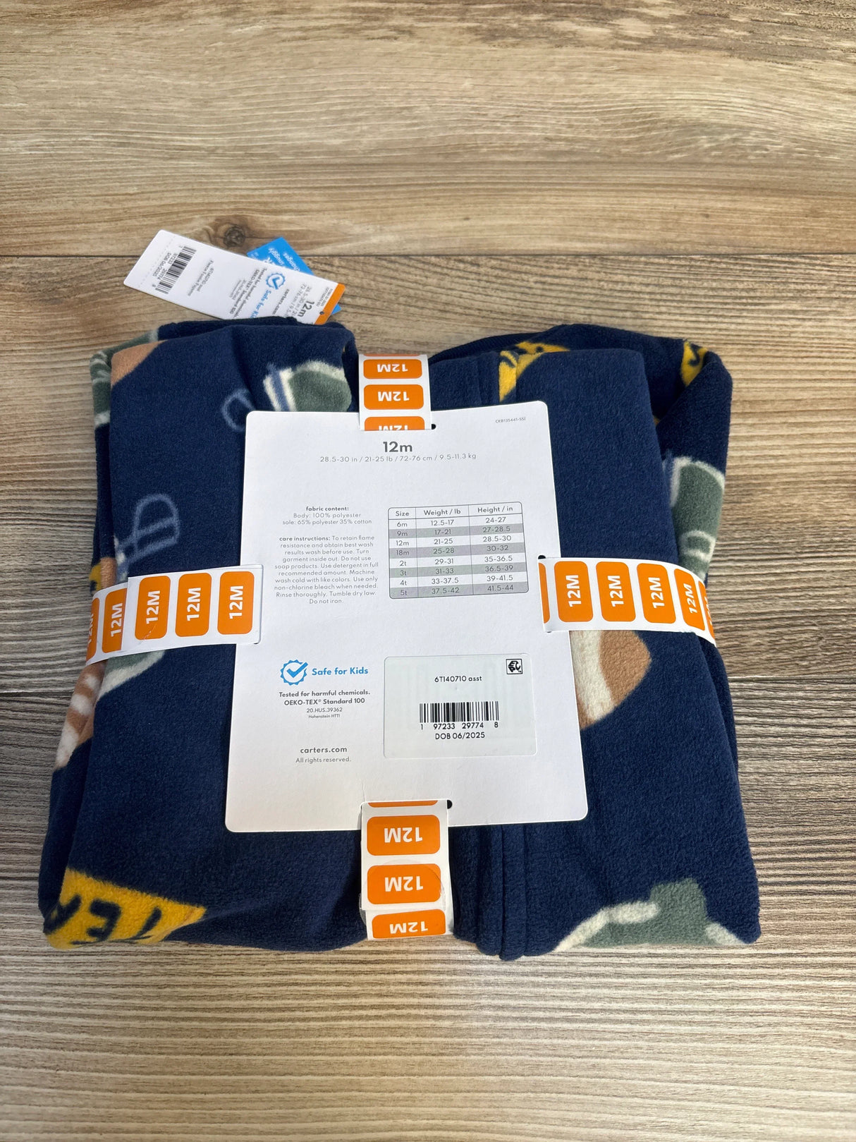 Folded navy blue baby fleece pajamas with football print, size 12 months, on wood surface