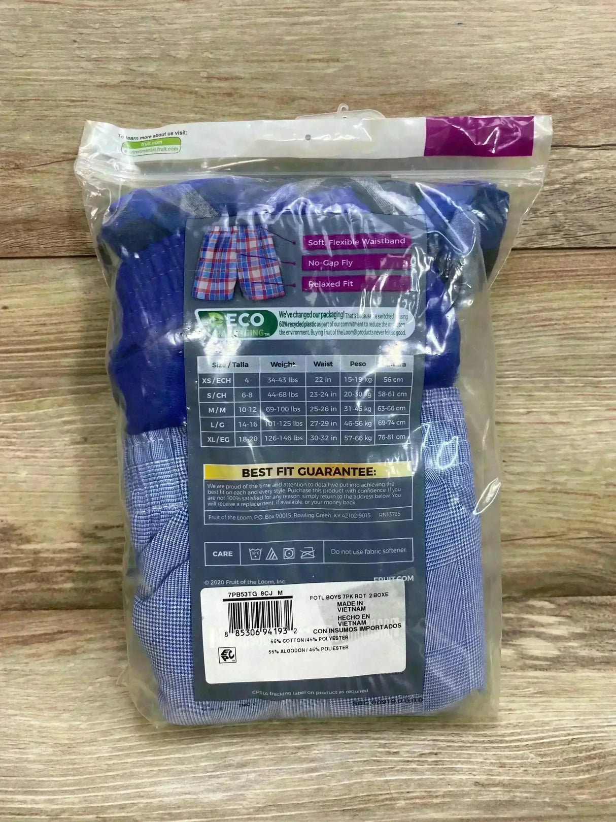 Front view of Fruit of the Loom 7-pack boys’ boxers in clear bag showing blue and plaid prints and ‘BEST FIT GUARANTEE’ on wood table