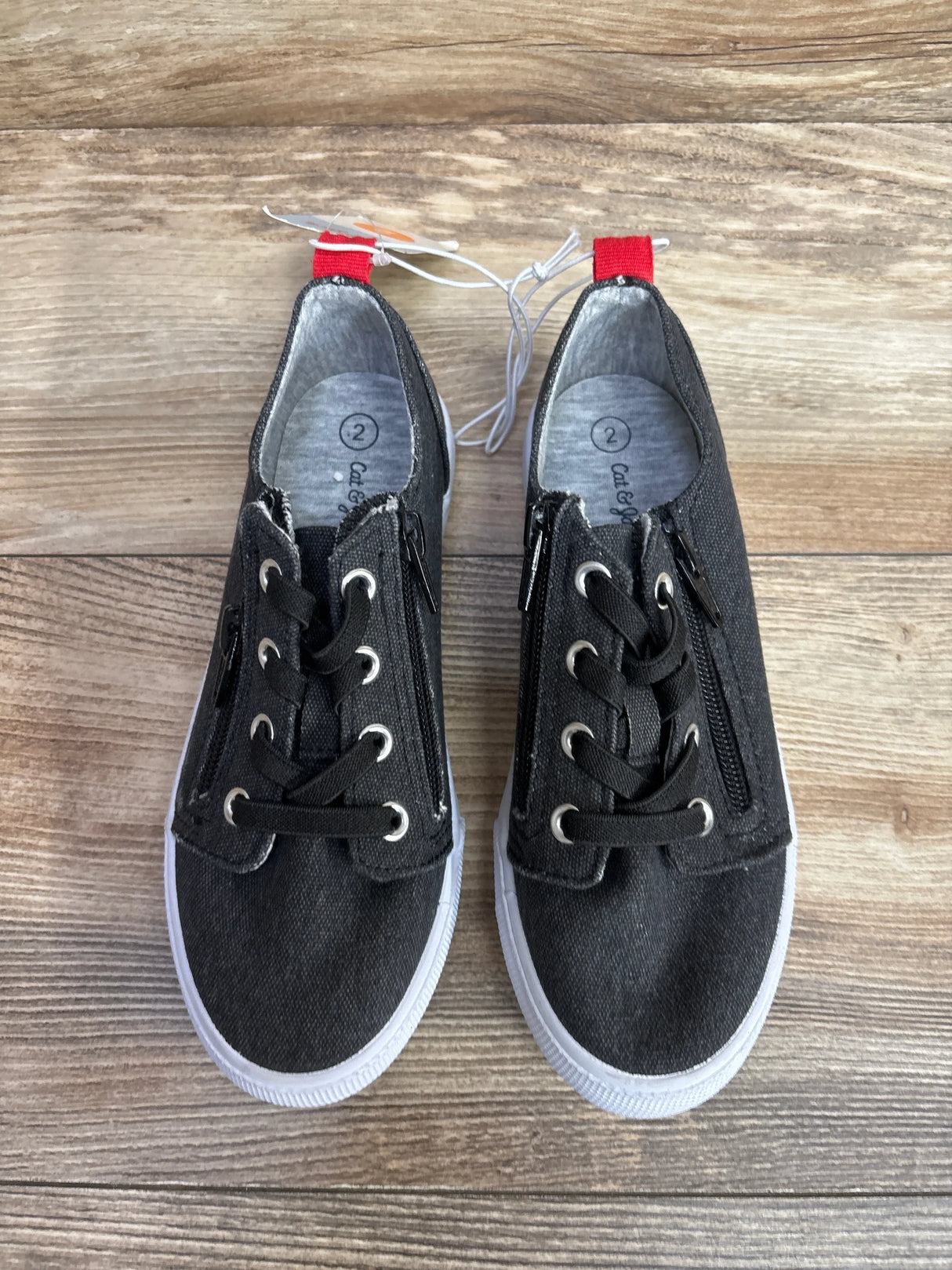 Pair of black toddler sneakers with white soles and red heel tabs on wooden floor