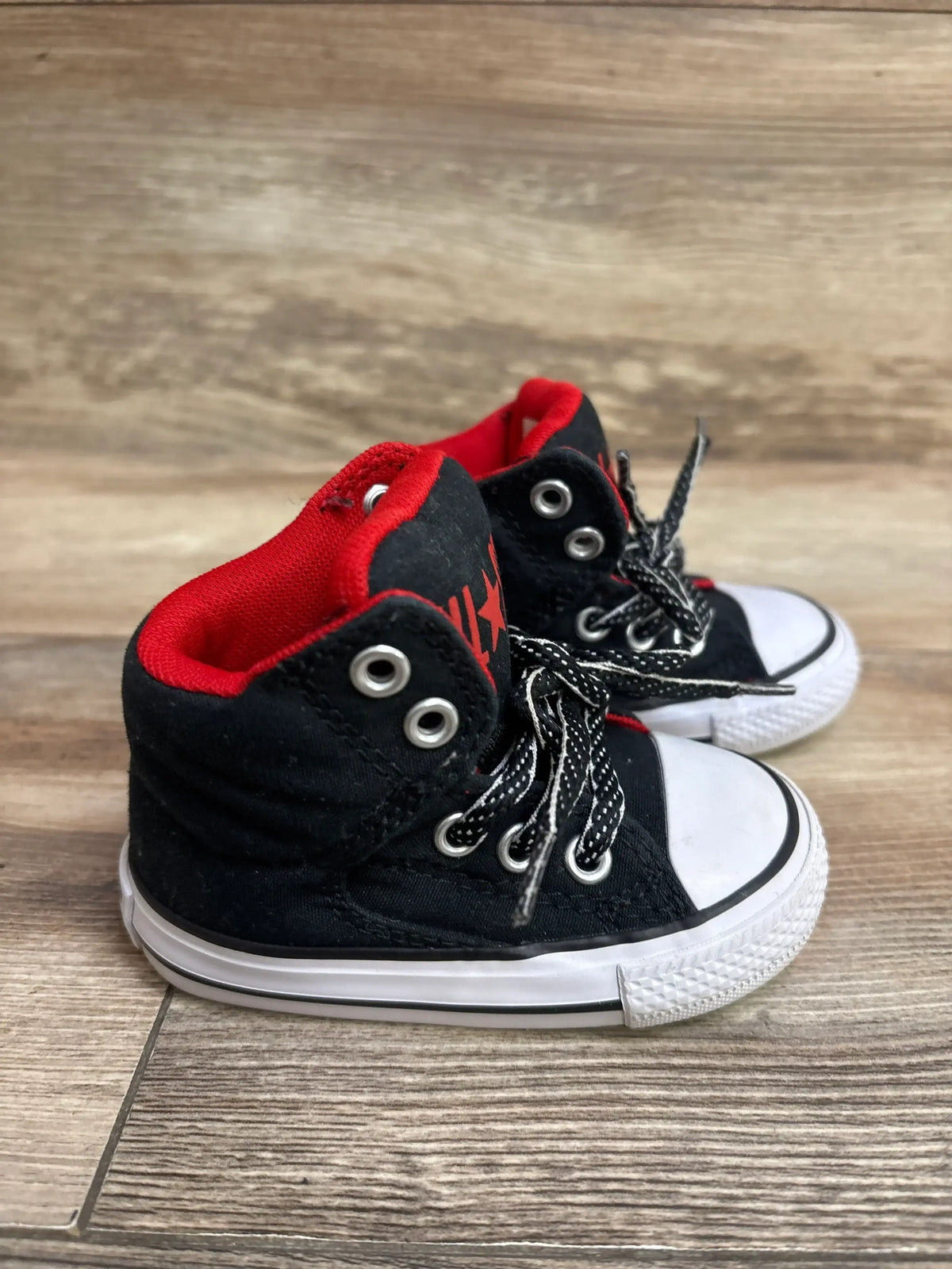 Angled view of Converse Chuck Taylor toddler high-top sneakers in black and red with white rubber toe caps on wood floor