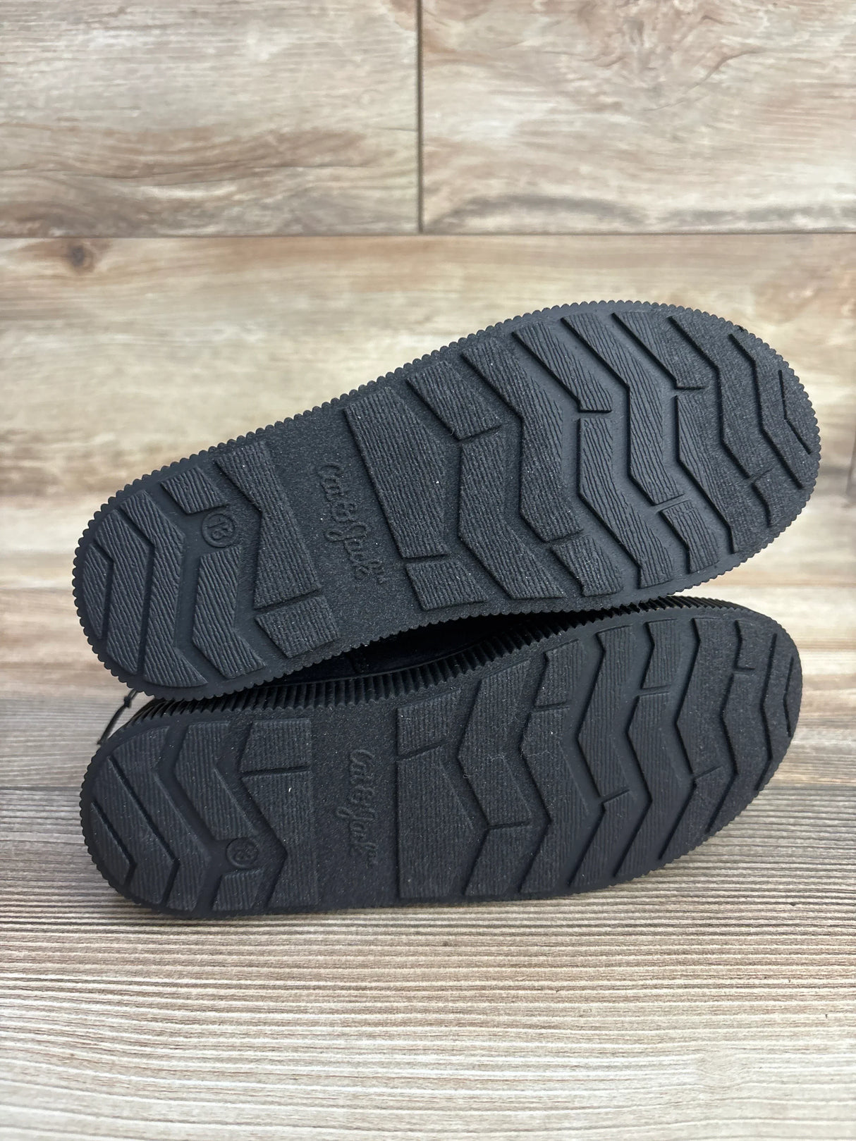 Bottom view of Cat & Jack Holland Shearling style toddler boots showcasing black treaded rubber soles with embossed Cat & Jack logo on wooden floor