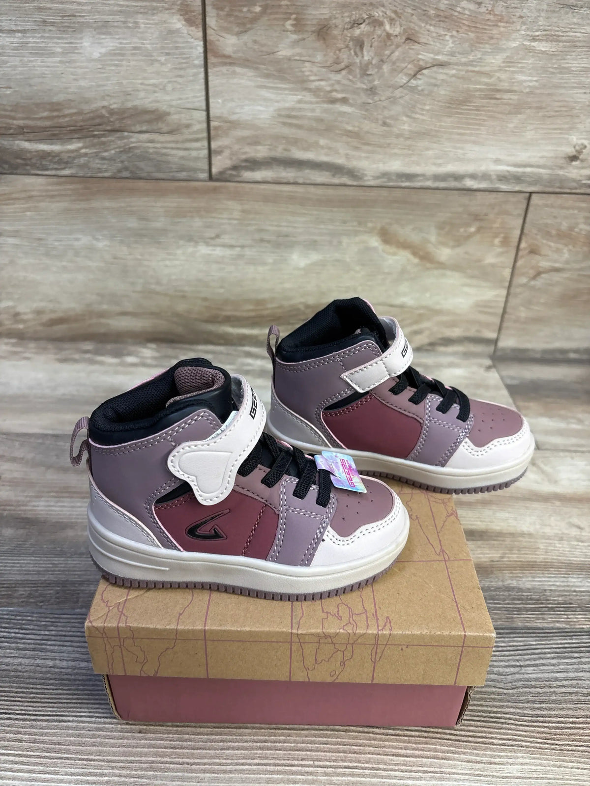 Three-quarter view of mauve toddler high-top sneakers showing hook-and-loop ankle strap and black laces on a shoebox