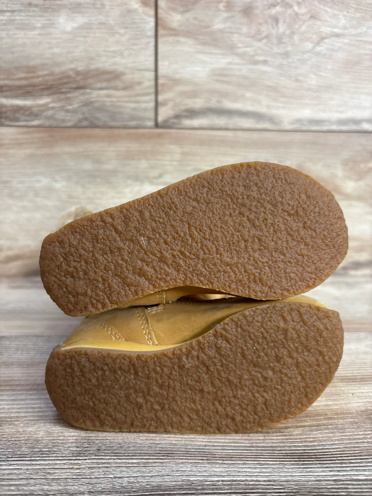 Stacked view of Timberland faux fur winter boots, tan toddler size 7C, showing crepe-style textured rubber outsoles on a wood background