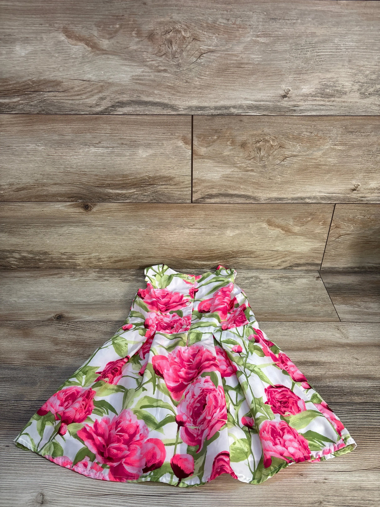 Girls floral dress with pink and green rose pattern on wooden floor background